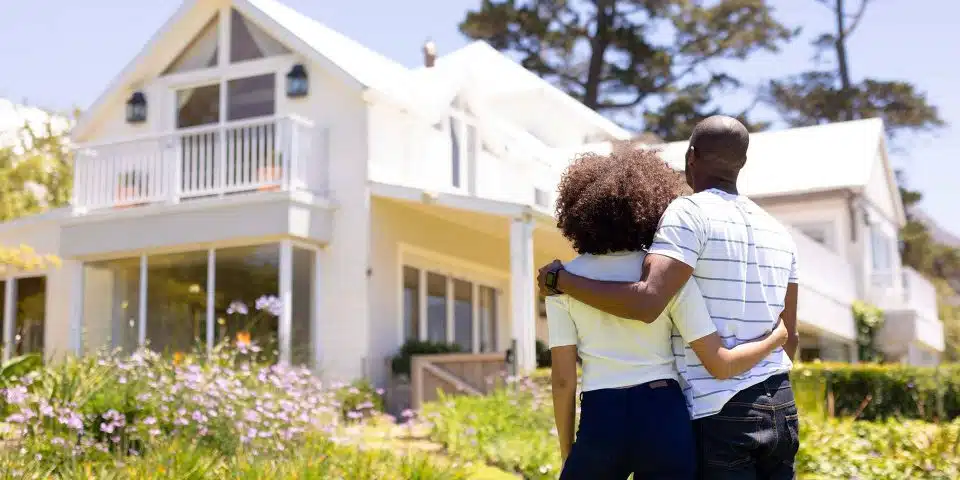 Black couple standing with their backs to the camera, hugging as they look at their new house